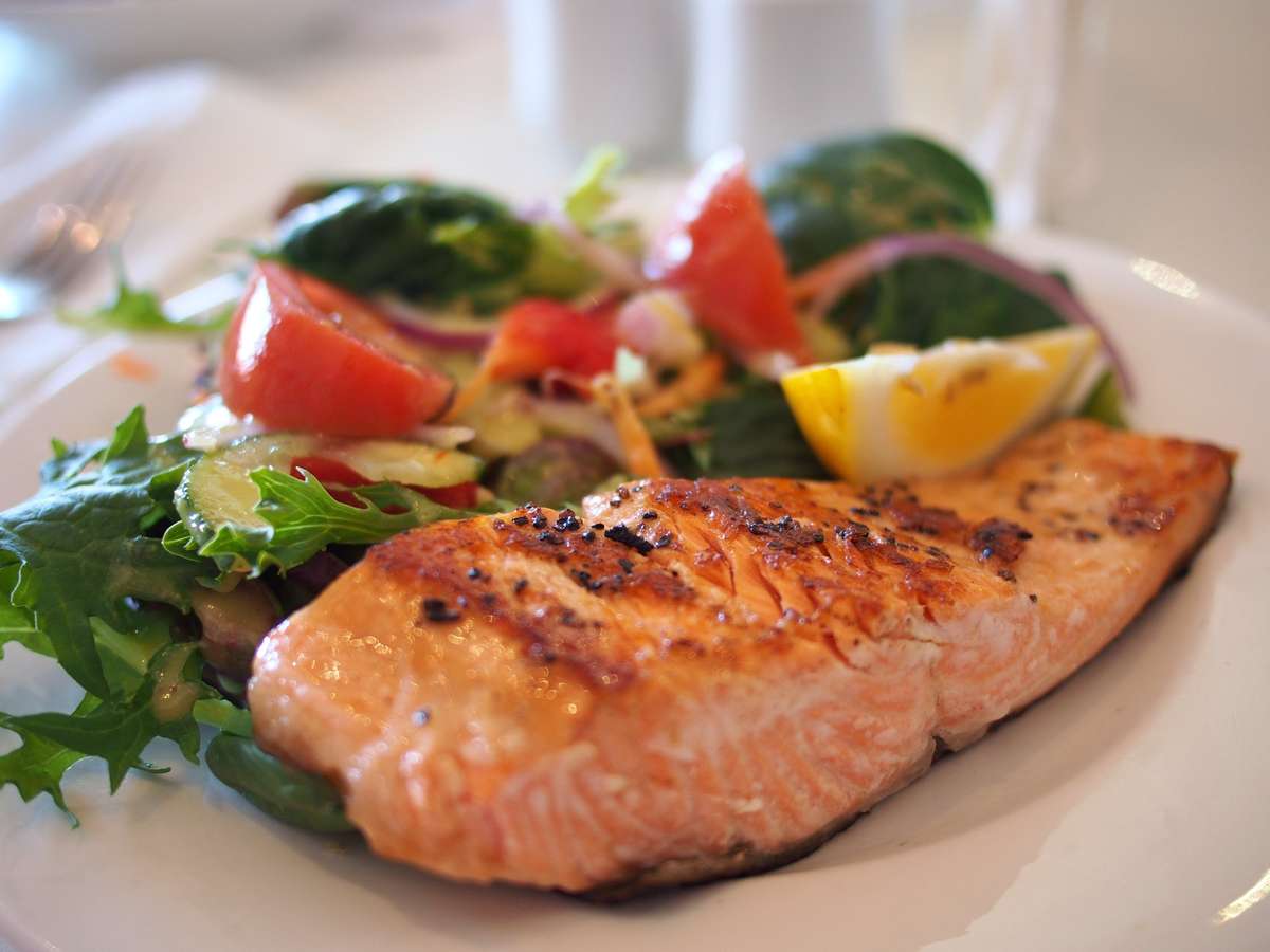 Grilled salmon fillet served with a fresh garden salad of mixed greens, tomatoes, cucumbers, and lemon wedge on a white plate.