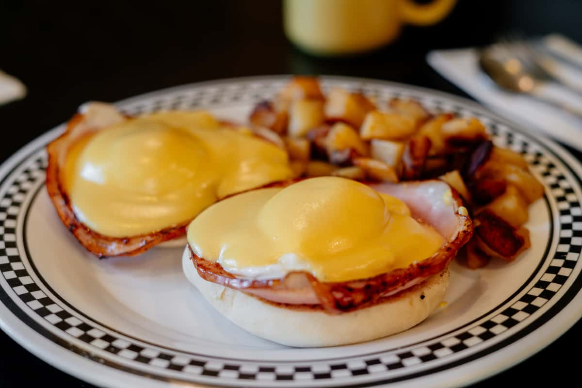 Two poached eggs, Canadian style bacon and tomato on top of a toasted Portuguese muffin and topped with hollandaise sauce