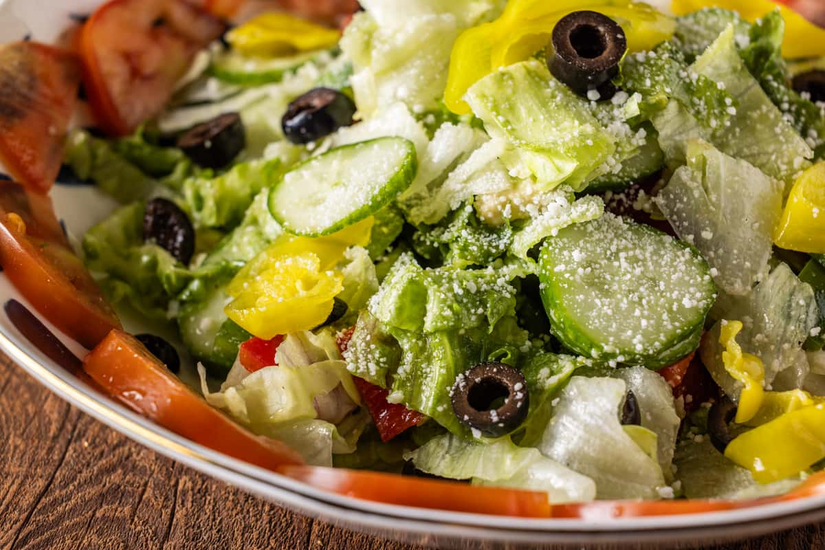 Fresh Italian chopped salad with crisp romaine lettuce, sliced cucumbers, black olives, yellow bell peppers, tomatoes, and grated Parmesan cheese served in a rustic bowl.