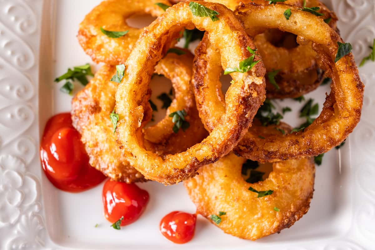 Crispy golden onion rings garnished with fresh parsley and served with ketchup on a white plate, classic pub-style appetizer.