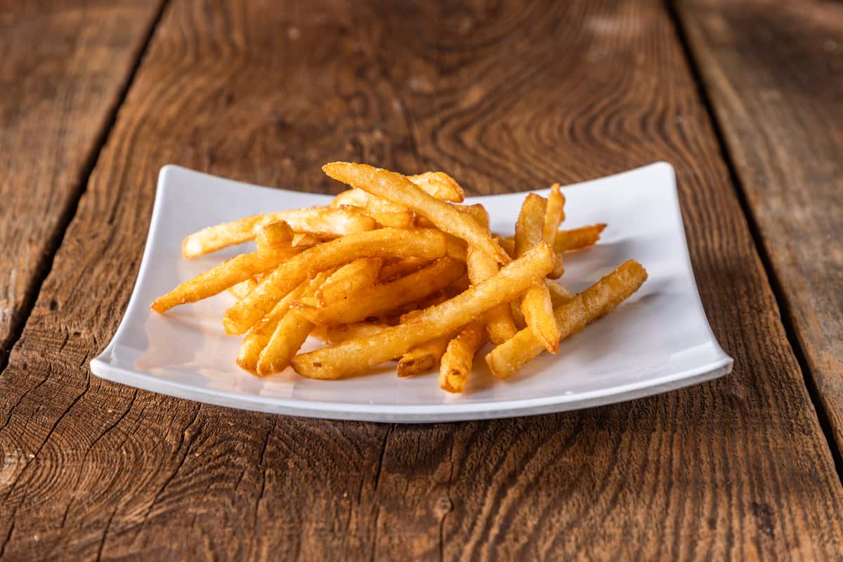 Crispy golden French fries served on a white plate over a rustic wooden table, classic restaurant-style side dish.