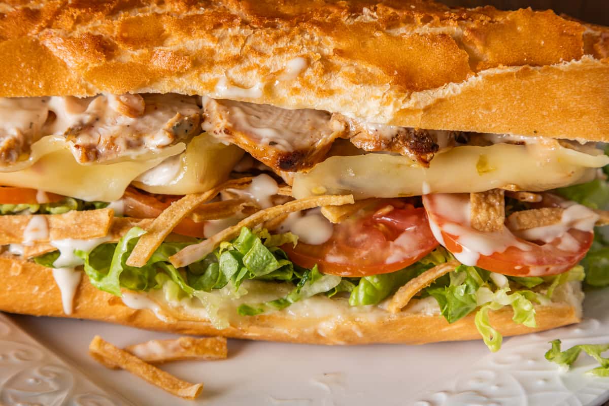 Grilled chicken sandwich on toasted French bread with melted provolone, fresh lettuce, sliced tomatoes, crispy potato sticks, and creamy garlic sauce for a hearty deli-style sub.