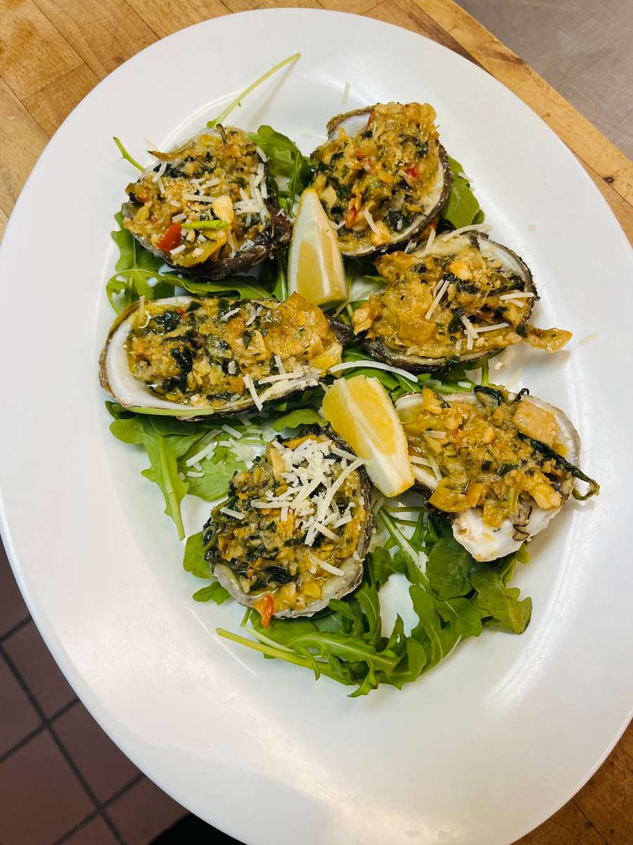 Six baked clams casino or oysters Rockefeller topped with cheese and served on a bed of bright green arugula and lemon wedges at Nataz restaurant.