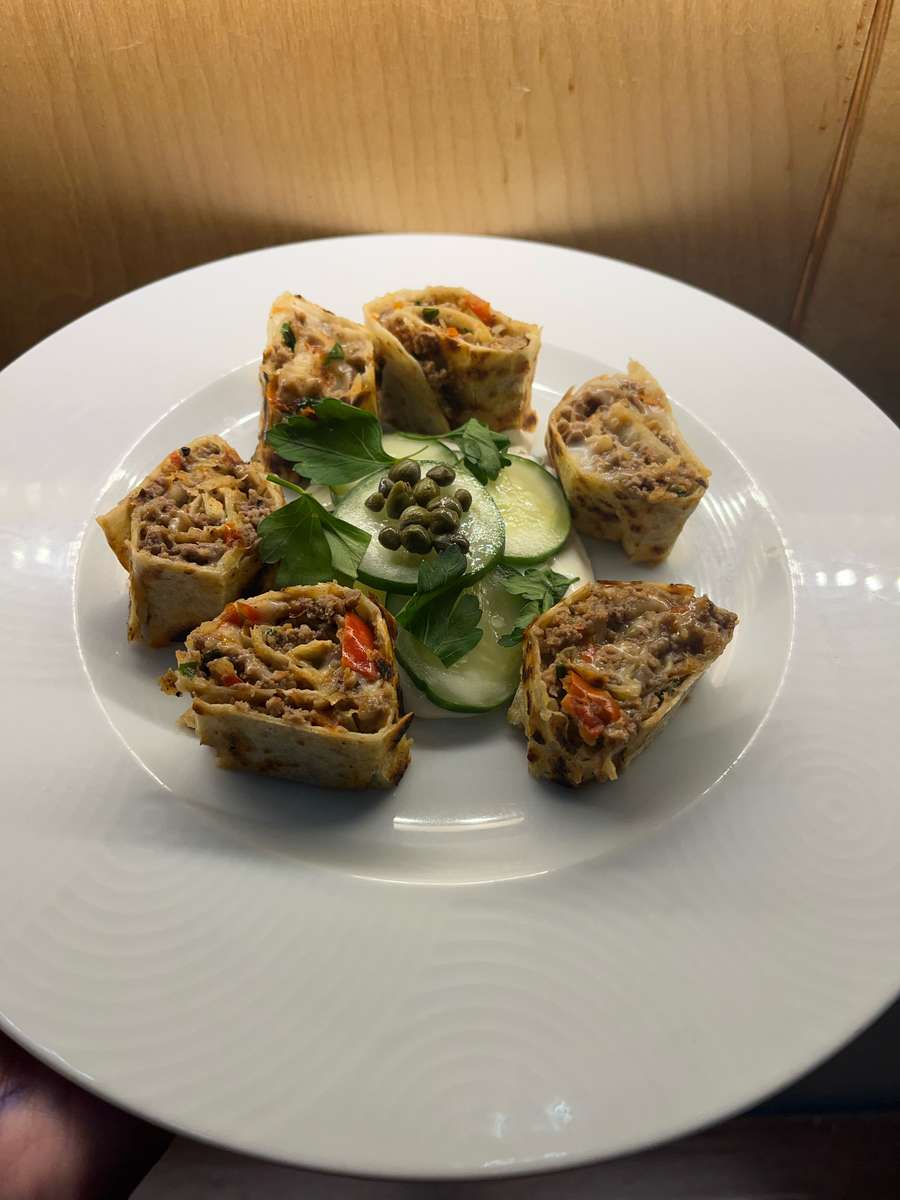 Brown savory stuffed pinwheel rolls garnished with green capers and cucumber on a white plate from Nataz.
