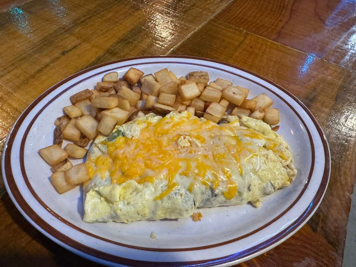 Cheese-covered omelet served with a side of golden diced breakfast potatoes on a white plate with a brown rim.