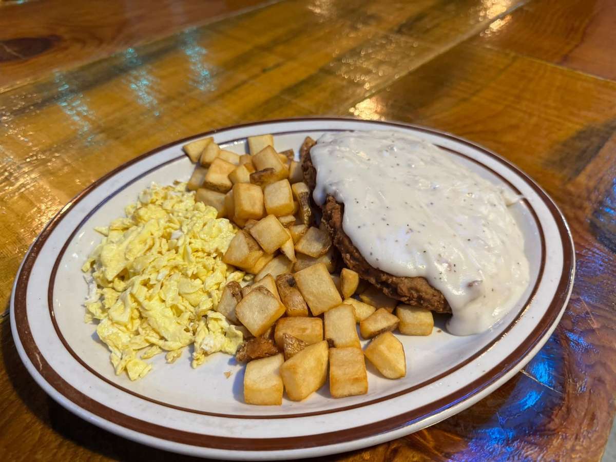 This plate features a hearty breakfast with scrambled eggs, cubed home fries, and chicken fried steak topped with creamy country gravy.