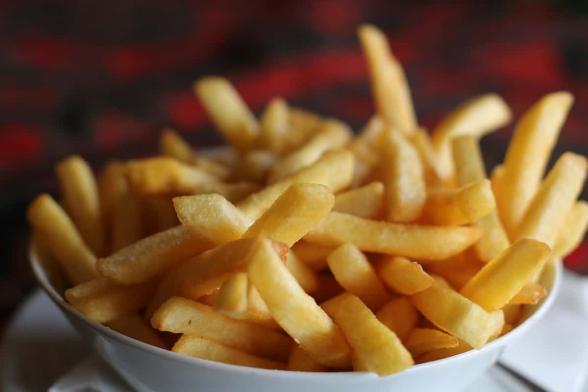 Golden crispy French fries served in a white bowl, showcasing a classic bar snack with a warm, casual pub-style presentation.