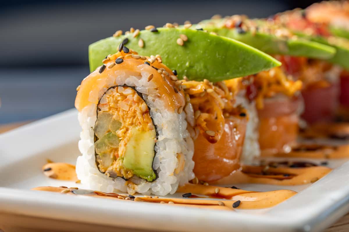 Sushi roll with signature crab mix, cucumber, and avocado, topped with fresh salmon and tuna, spicy kanikama, avocado, sriracha, spicy mayo, eel sauce, and sesame seeds