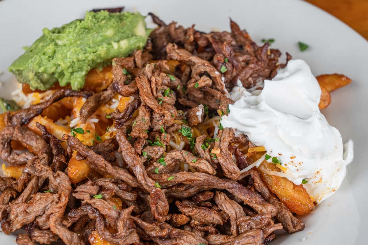 Seasoned beef fajita fries topped with grilled meat, guacamole, and sour cream.