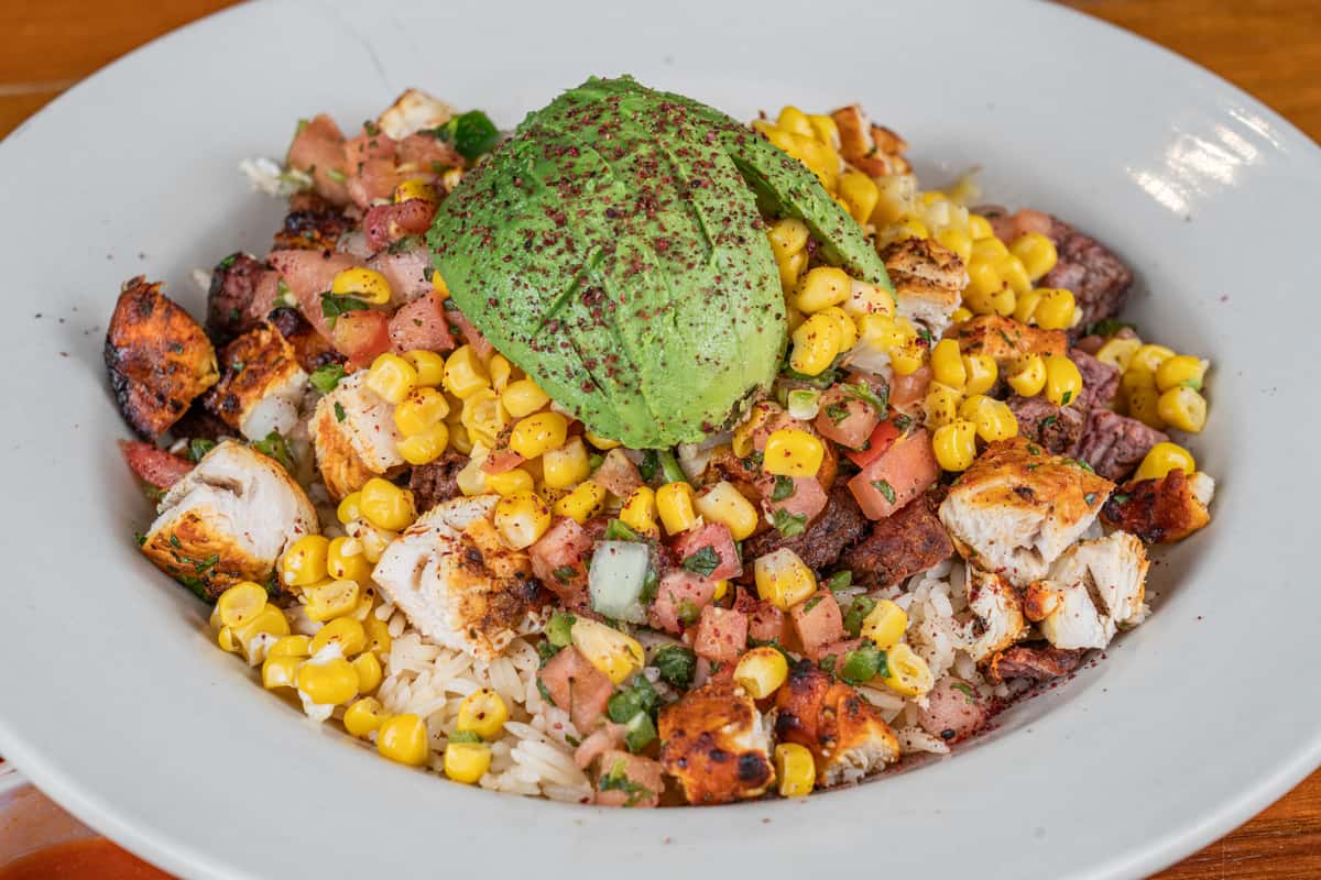 Colorful grilled chicken bowl with corn, beans, vegetables, guacamole, and fresh toppings.