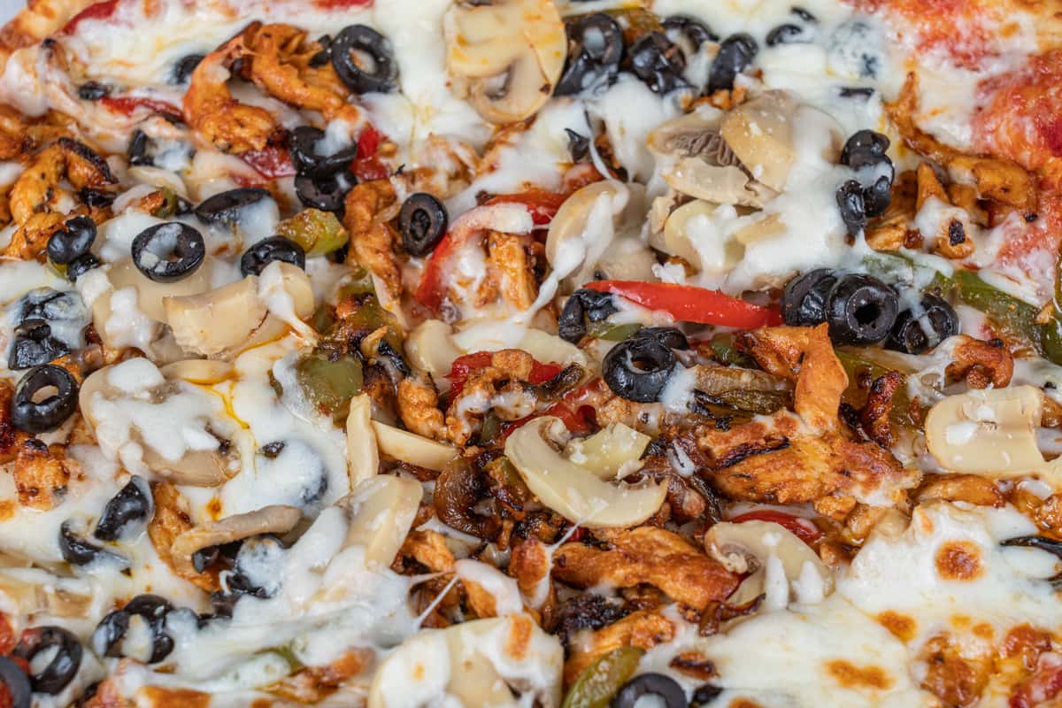 Close-up of pizza topped with seasoned chicken, vegetables, olives, and melted cheese.