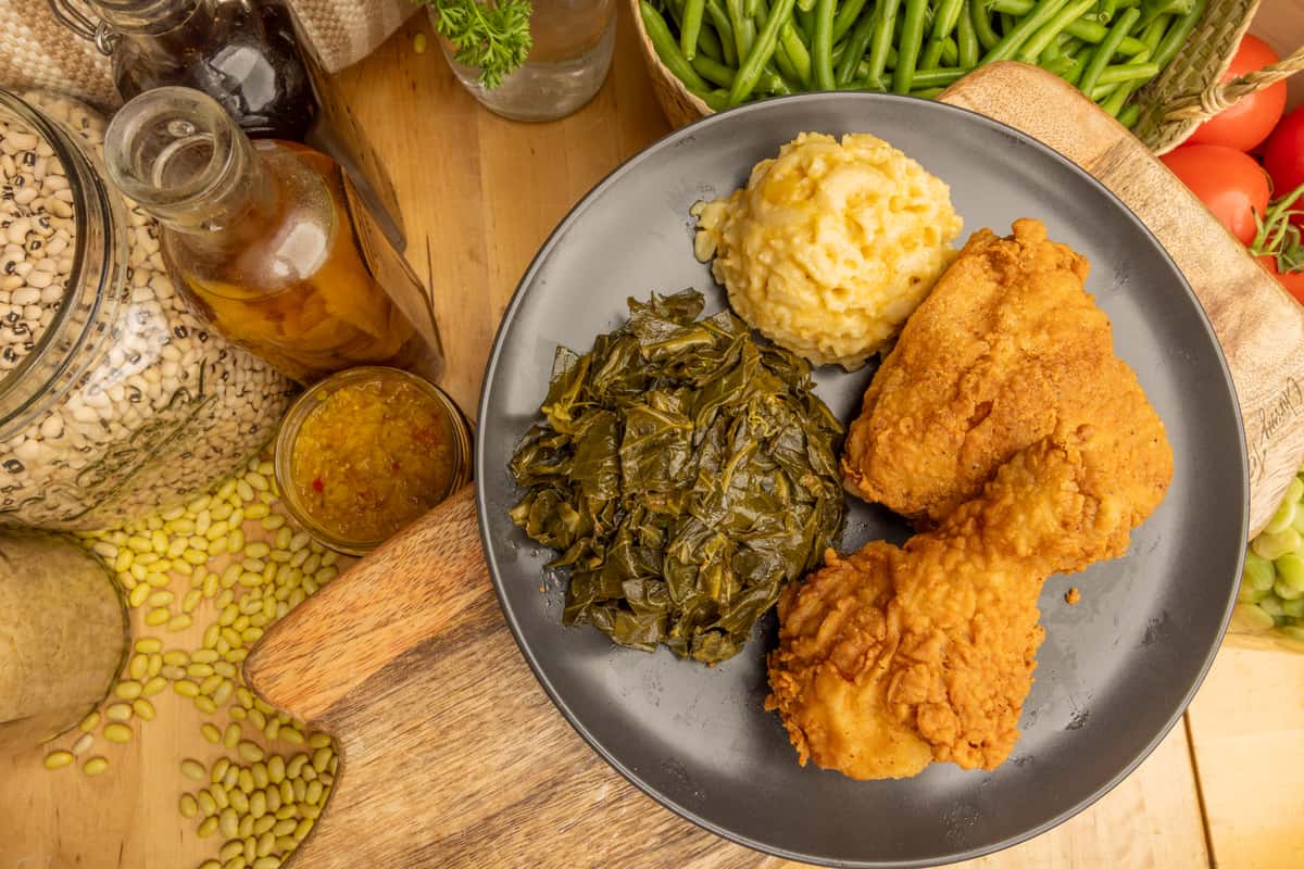 Crispy fried chicken with collard greens and mashed potatoes on a plate, fresh greens in background