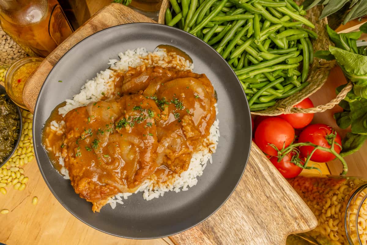 Overhead view of smothered chicken in brown gravy over white rice, with green beans and tomatoes nearby.