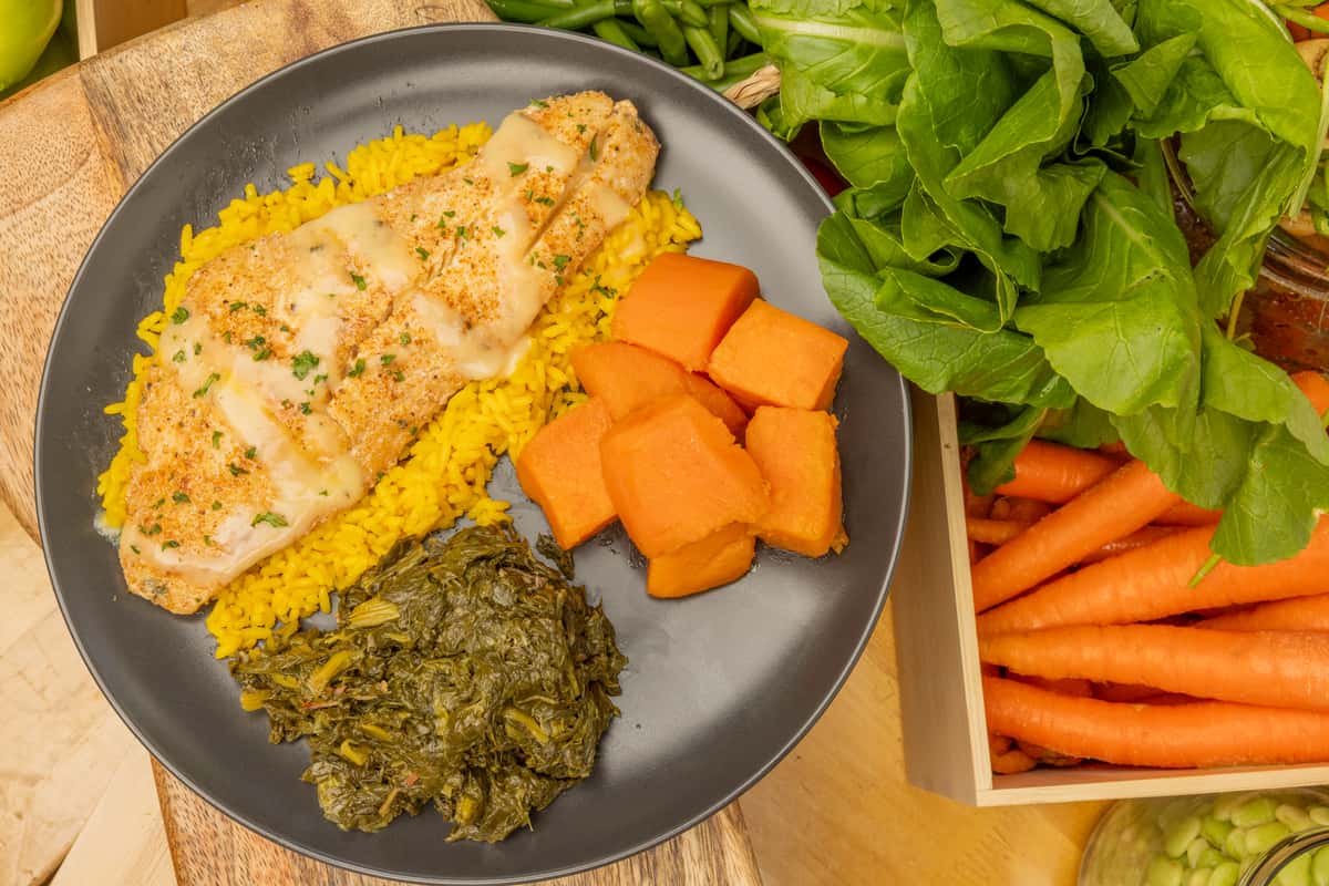 Grilled fish topped with light sauce over yellow rice, served with collard greens and sweet potato chunks.