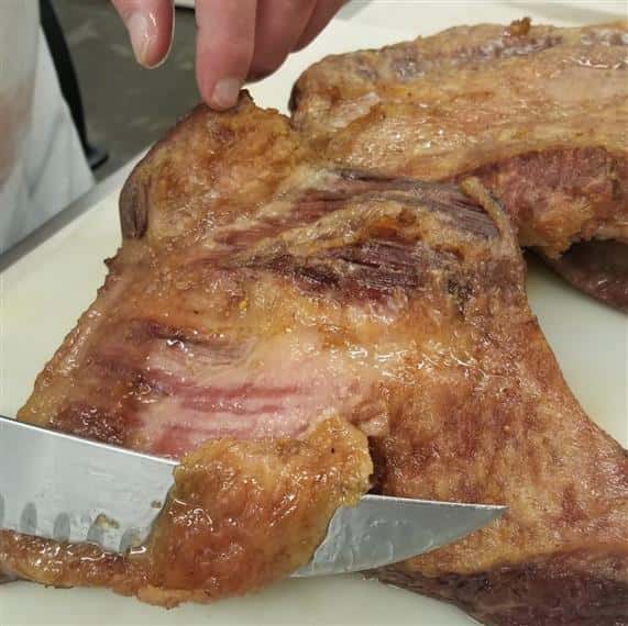 butcher knife cutting into a slab of cooked pork