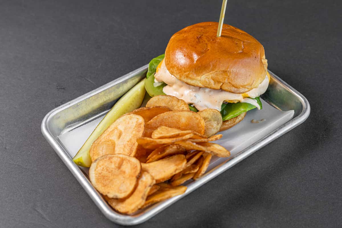 USDA Black Angus cheeseburger with lettuce and tomato served with house chips and pickle on metal tray
