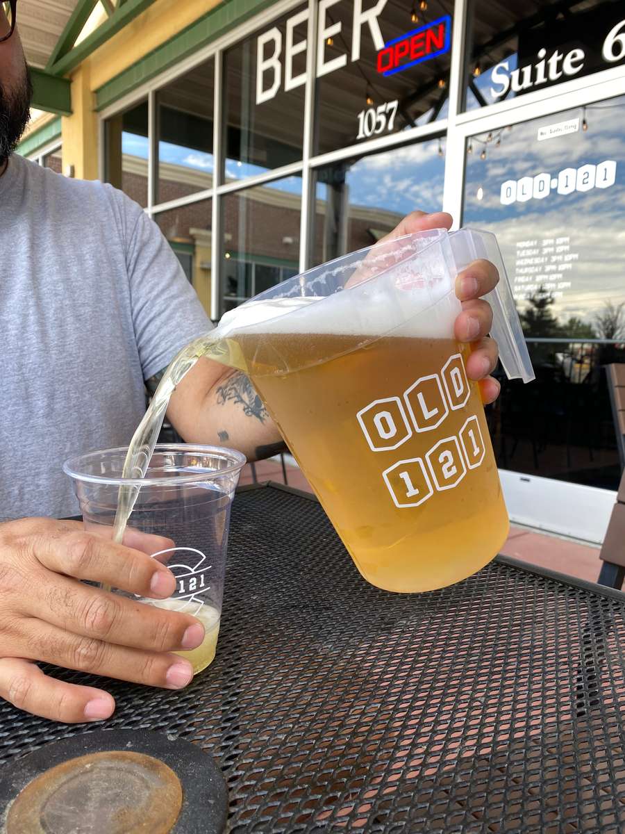 Close-up of a customer pouring golden beer from an Old 121 pitcher into a plastic cup on the outdoor patio.