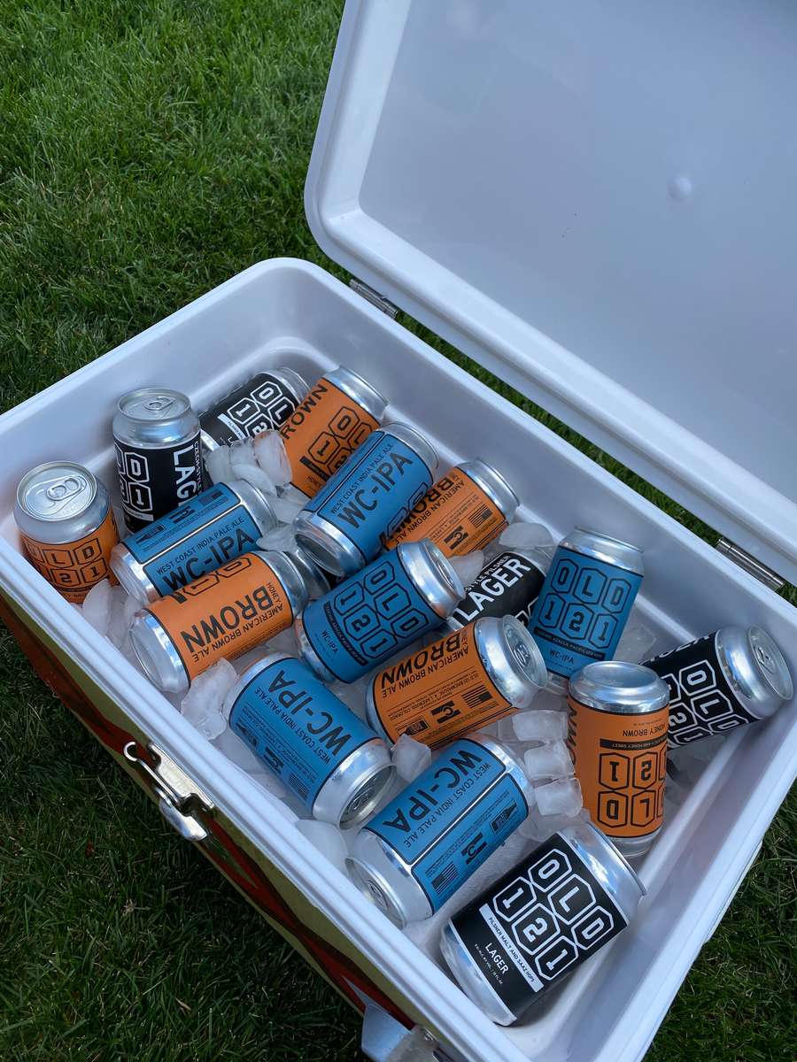 Ice-filled cooler packed with colorful Old 121 beer cans, including West Coast IPA, Lager, and Brown Ale.
