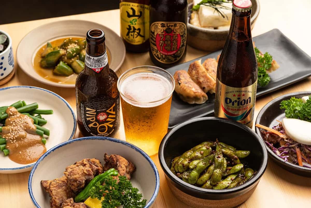 Assortment of Japanese dishes and beer. Fried chicken, green beans with sauce, edamame, and gyoza on a wooden table.