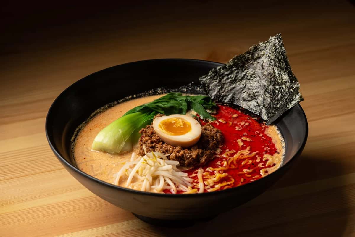 Ramen bowl with creamy broth, seasoned ground pork, yellow noodles, half a boiled egg, bok choy, bean sprouts, and nori.