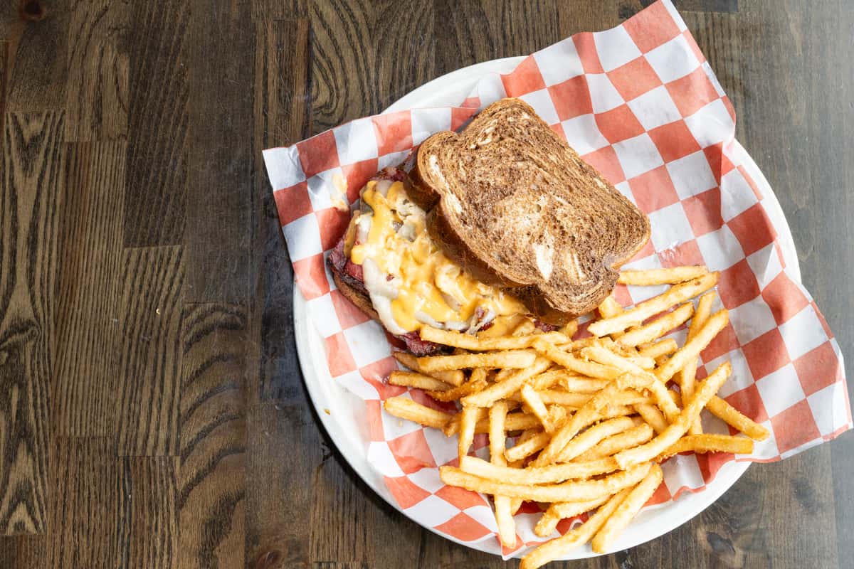 grilled sandwich with melted cheese and smoked meat served with crispy fries in a red checkered basket at a casual smokehouse
