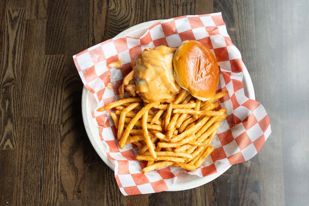 cheeseburger with melted cheese sauce and crispy fries served in a red checkered basket at a casual smokehouse restaurant