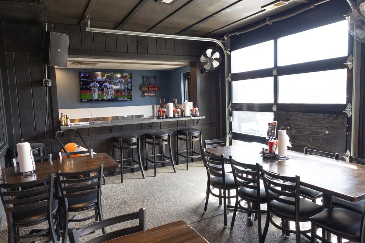 casual bar seating area with high stools, wall-mounted TV, and garage-style windows in a relaxed smokehouse restaurant