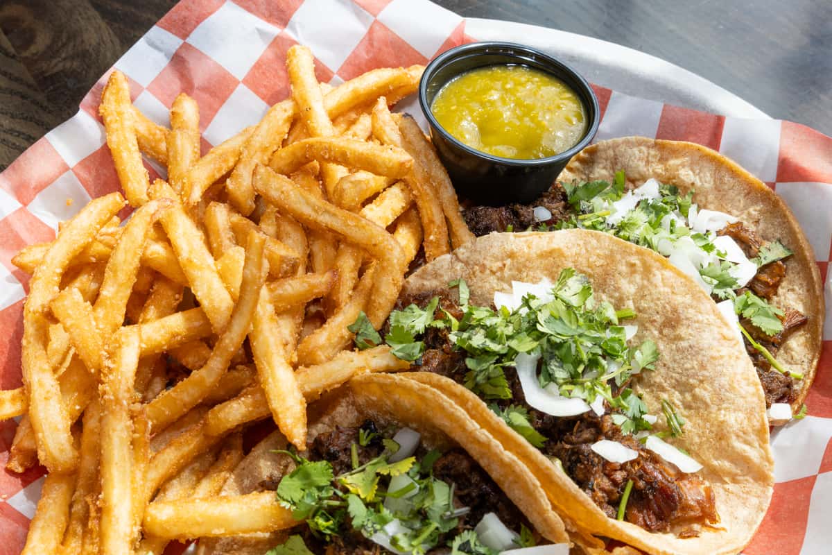 Street-style tacos with chopped beef, onions, cilantro, and lime, served with crispy French fries and salsa