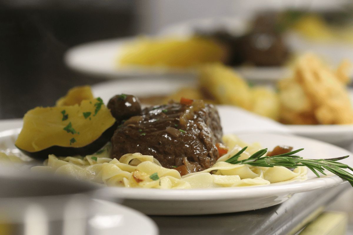 Plated meal of braised beef, tagliatelle pasta, acorn squash, and a sprig of rosemary.