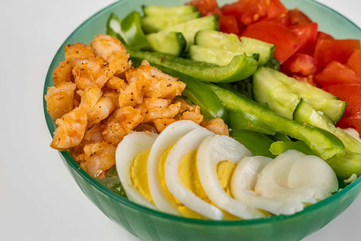 Colorful shrimp salad bowl featuring seasoned shrimp, sliced hard-boiled eggs, bell peppers, cucumbers, tomatoes, and onions—fresh and nutritious Caribbean-inspired meal.