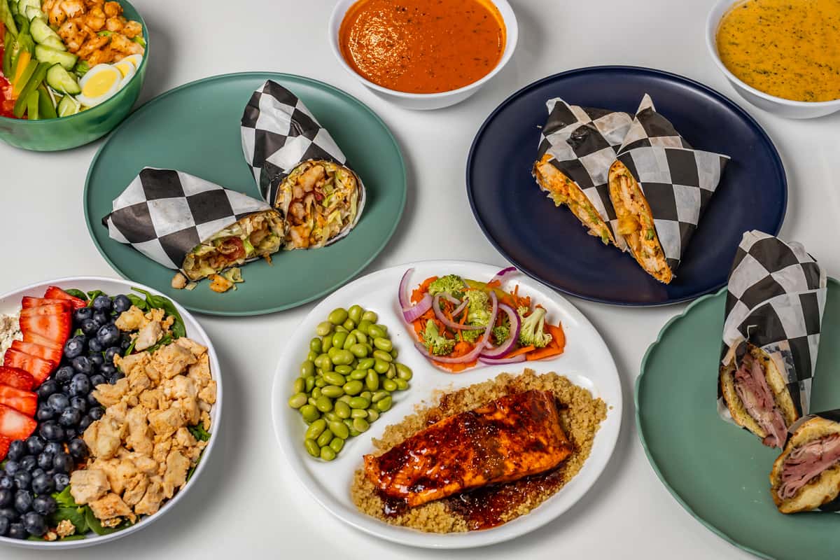 Healthy Caribbean fusion meal spread with wraps filled with grilled meats, salmon over quinoa with edamame and veggies, vibrant fruit and chicken salad, shrimp salad bowl, and sides of tomato and mustard-based sauces—colorful, nutritious Latin-inspired cuisine.
