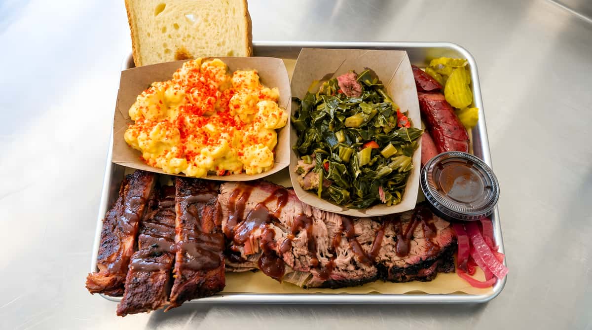 BBQ platter with ribs, brisket, mac and cheese, collard greens, pickles, and red onions.