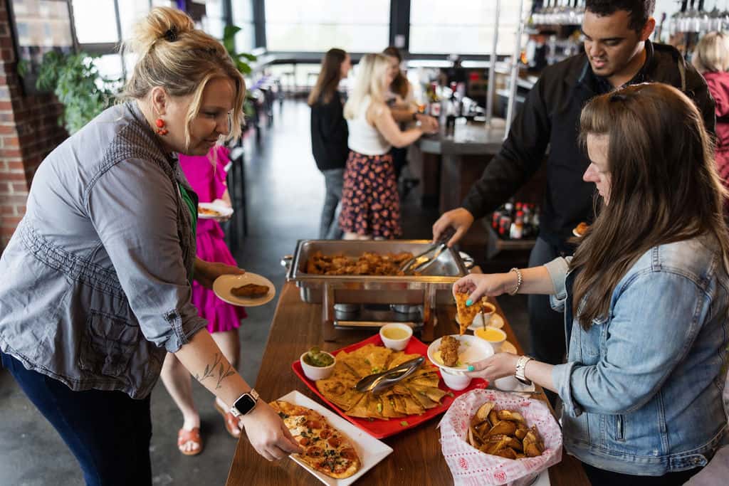 Staff members serving food at a catered event to attendees in a food line