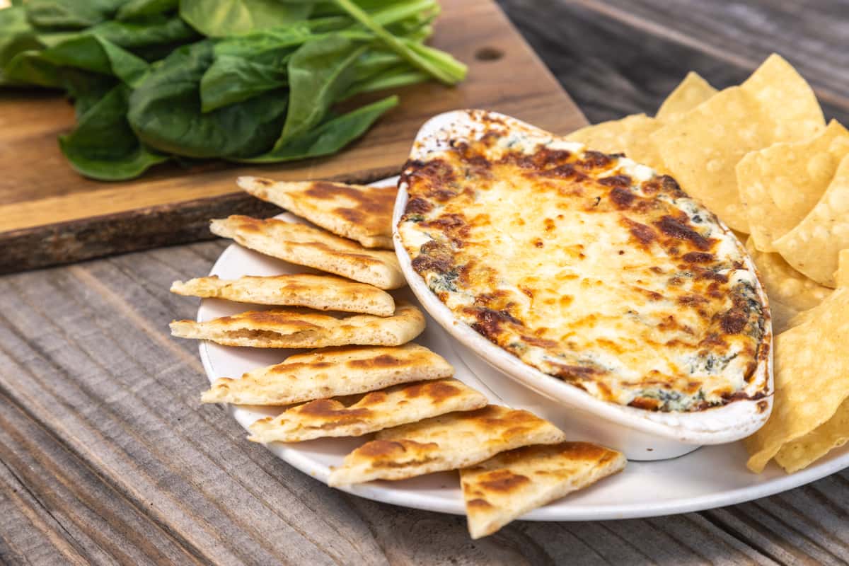 A platter of cheesy dip with slices of pita bread