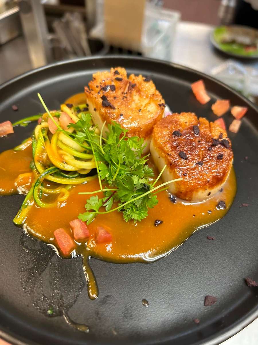 Seared scallops with zucchini noodles, fresh herbs, and diced tomatoes in a vibrant orange sauce.