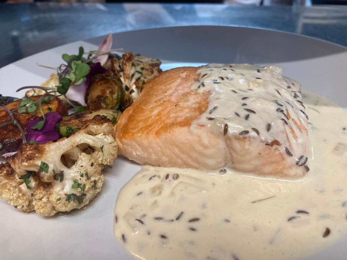 Pan-seared salmon with wild rice cream sauce, served with roasted cauliflower, Brussels sprouts, and microgreens.