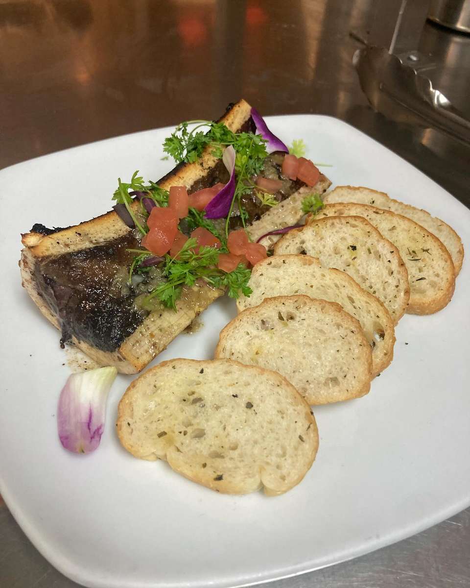 Roasted bone marrow garnished with herbs and diced tomato, served with toasted crostini on a white plate.