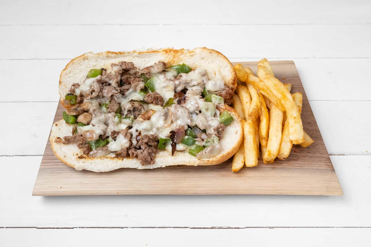 Opened up Philly Steak sandwich next to dries on a wooden board