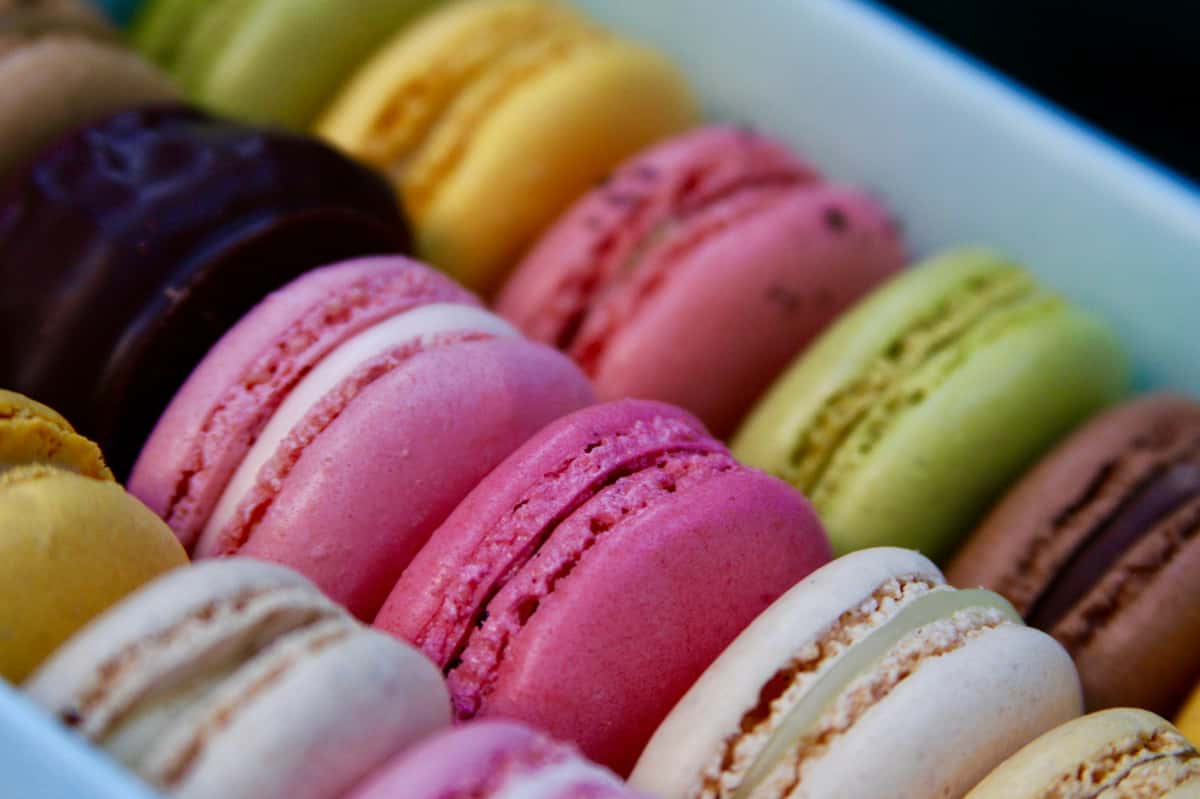 An assortment of colorful macarons in pink, yellow, green, brown, and cream, each with a delicate filling sandwiched between the light, crisp shells.