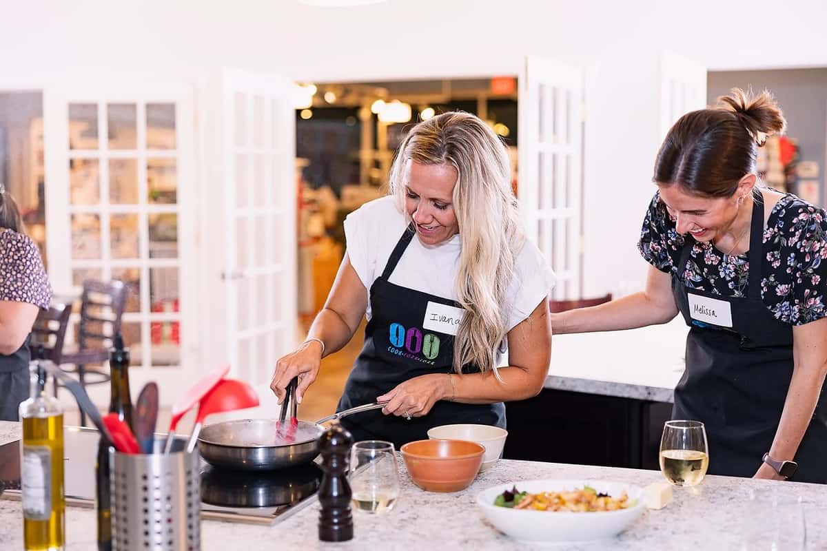 Adults enjoying a hands-on cooking class, preparing a meal together in a bright culinary studio while learning cooking techniques and sharing wine.