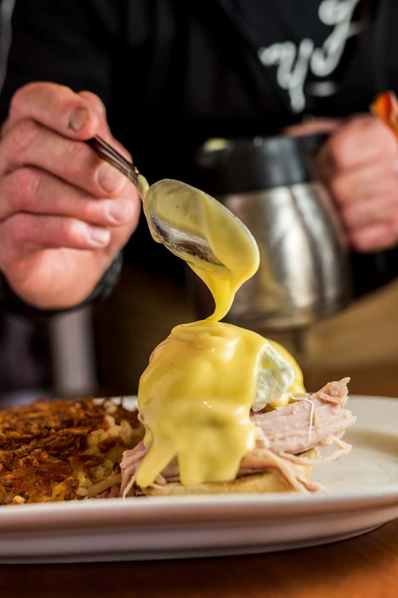 Person covering eggs benedict with hollandaise sauce