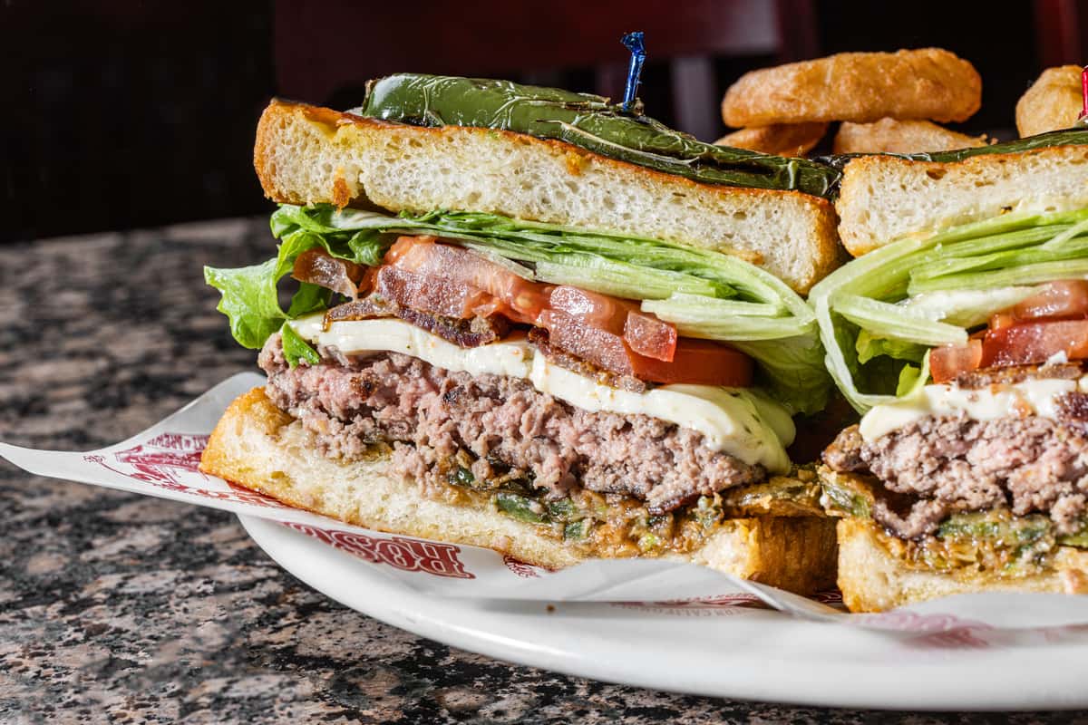 club sandwich stacked with bacon, lettuce, tomato, and deli meat served with pickle garnish