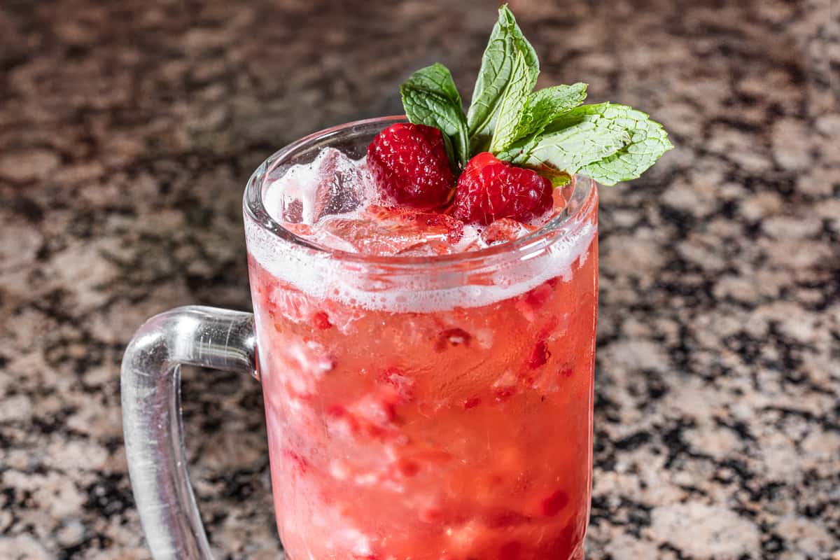 berry cocktail with raspberries, mint garnish, and crushed ice served in a frosty mason jar mug