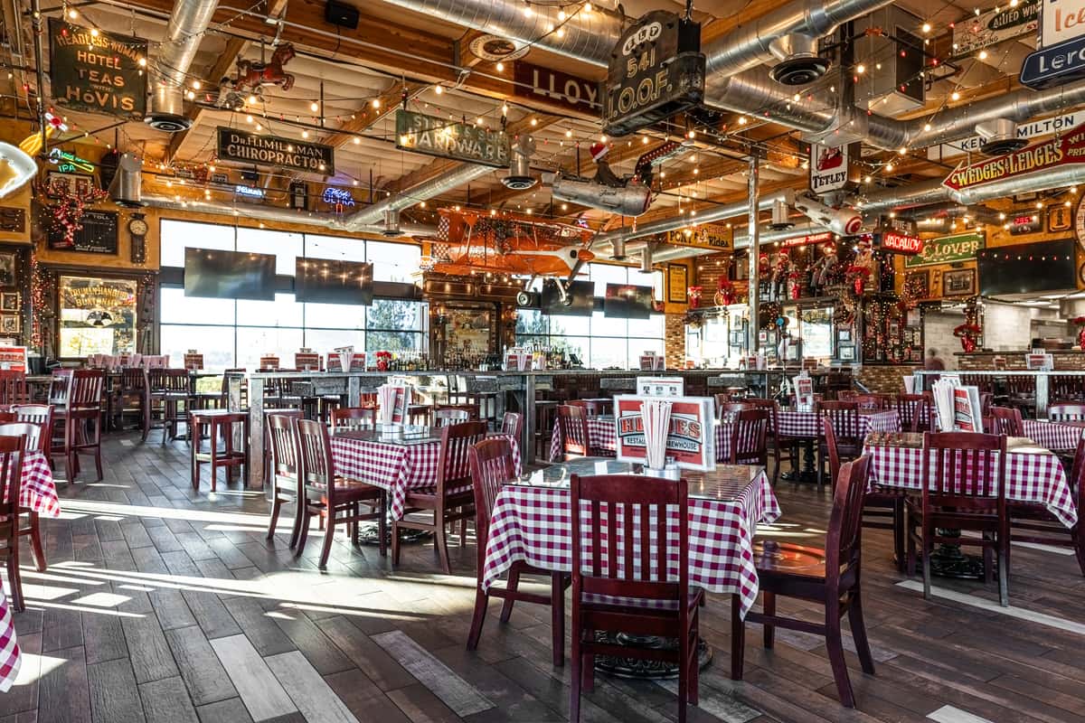 rustic restaurant dining room with checkered tablecloths, exposed wood beams, and warm string lighting throughout the space
