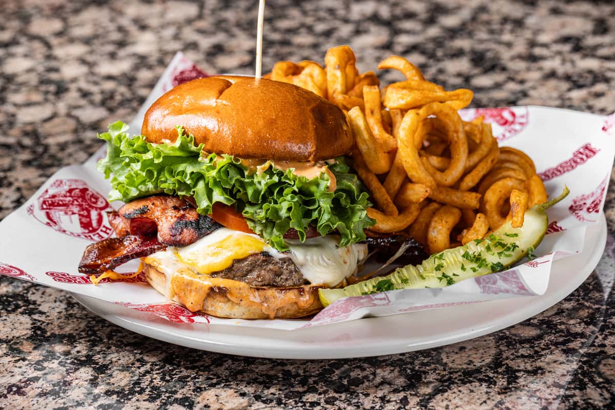 stacked bacon cheeseburger with lettuce, tomato, onion rings, and curly fries served on a rustic plate