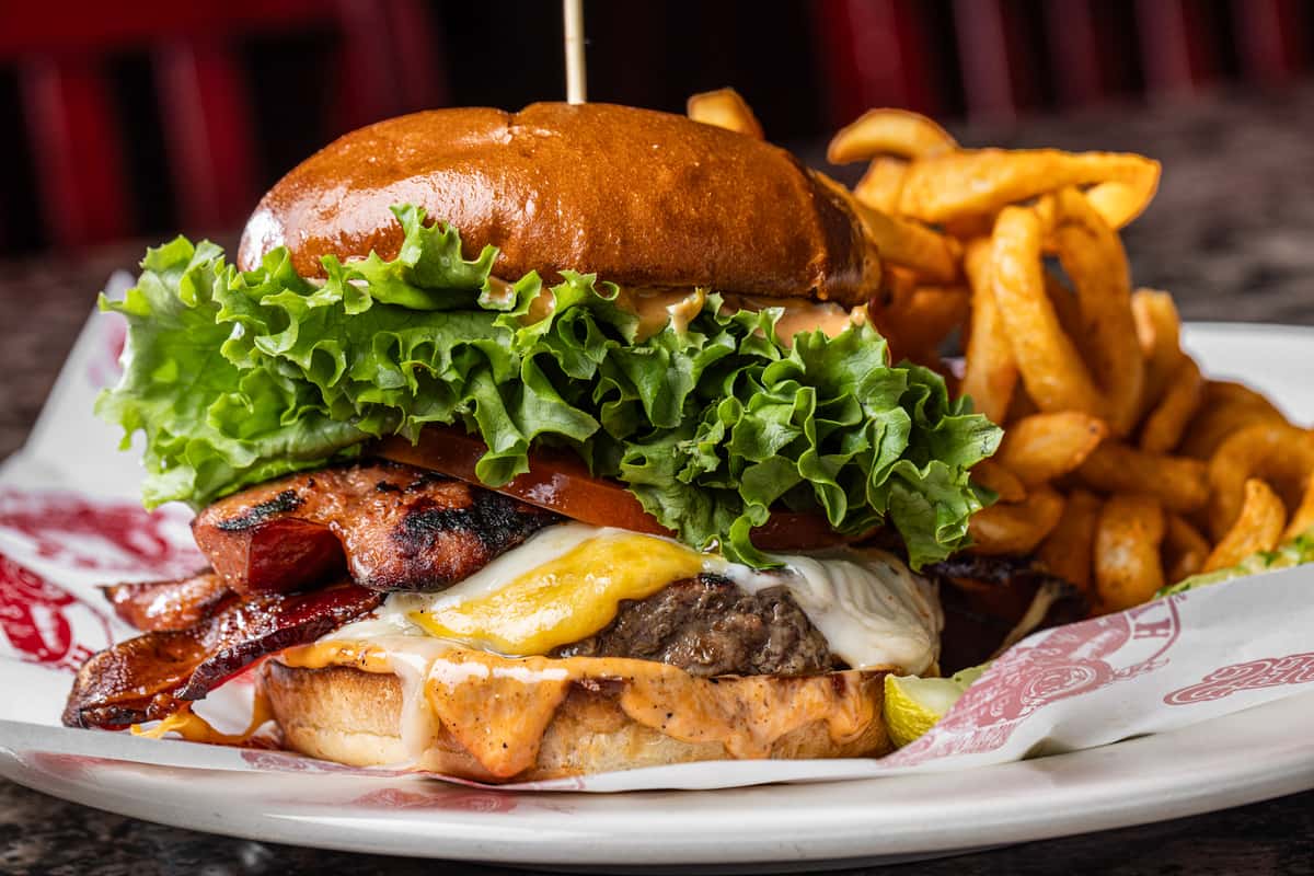 stacked bacon cheeseburger with melted cheese, fresh lettuce, and curly fries served on a rustic plate