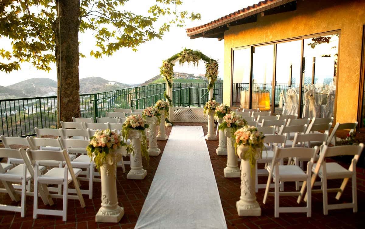 Outdoor wedding ceremony setup with floral aisle arrangements, white folding chairs, and mountain views at a romantic hillside venue