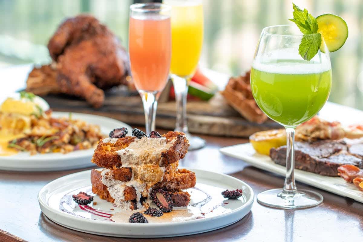 Savor the moment with French toast topped with fruit and syrup on a pristine table, surrounded by vibrant brunch cocktails at Orange Hill