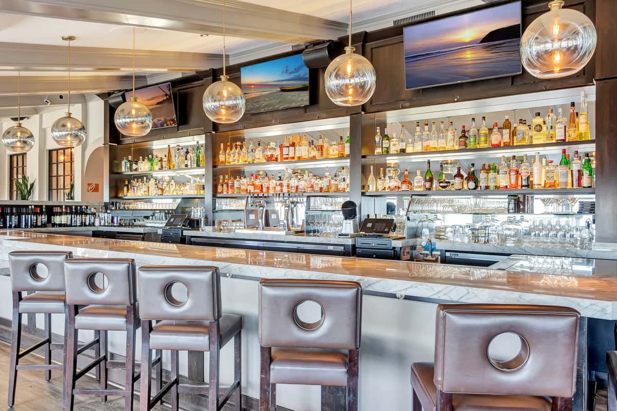 Chic brown leather bar stools contrast with brightly lit liquor shelves, creating a stylish ambiance.