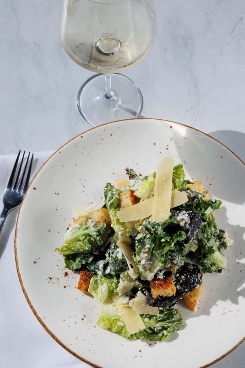 Fresh green ingredients topped with Parmesan, paired elegantly with a glass of white wine.